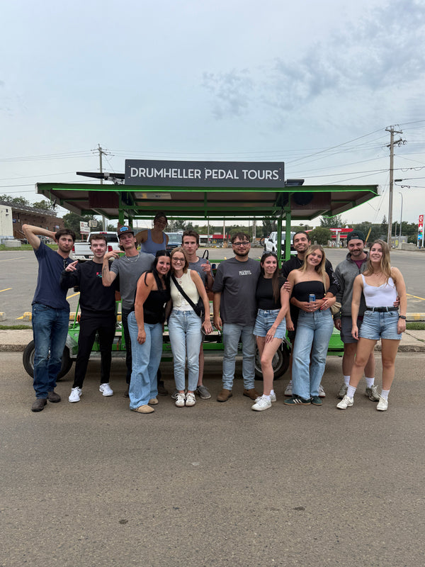 Group of people posing for a photo in front of Drumheller Pedal Tours sign.